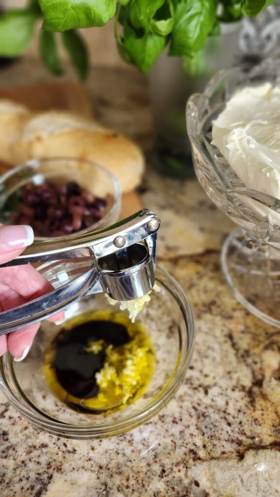 hand holding garlic press over a bowl of olive oil