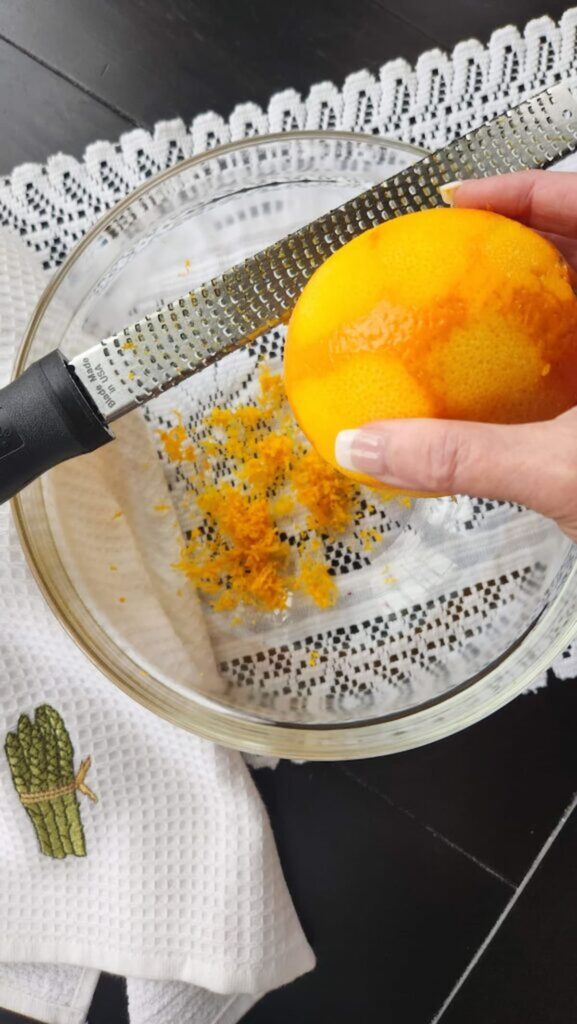 orange being zested over a glass bowl
