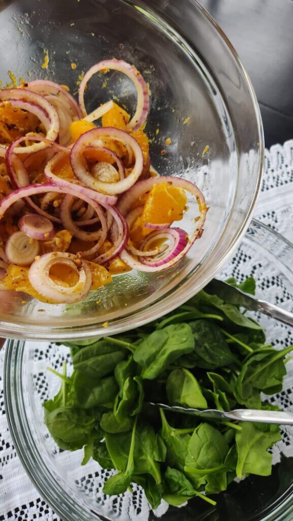 onion, orange, walnuts in glass bowl with spinach leaves on side