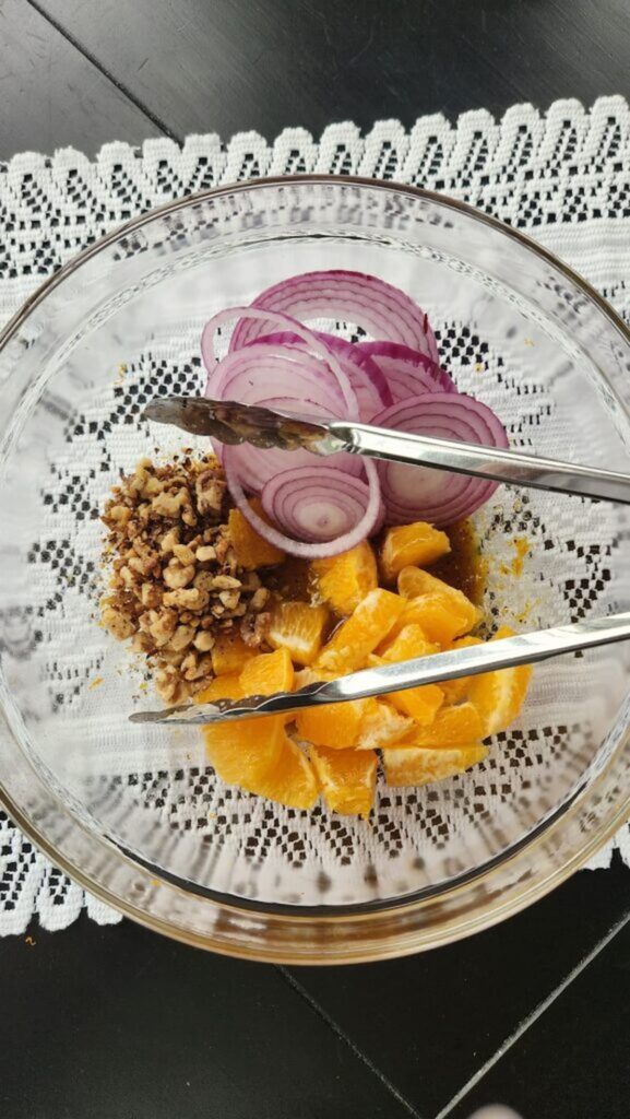 adding red onion, orange and walnuts in bowl